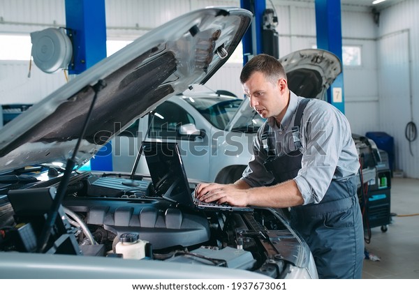 car mechanic\
using a computer laptop to diagnosing and checking up on car\
engines parts for fixing and\
repair