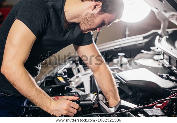 Car mechanic using electrical tool for testing car\
system in garage repair