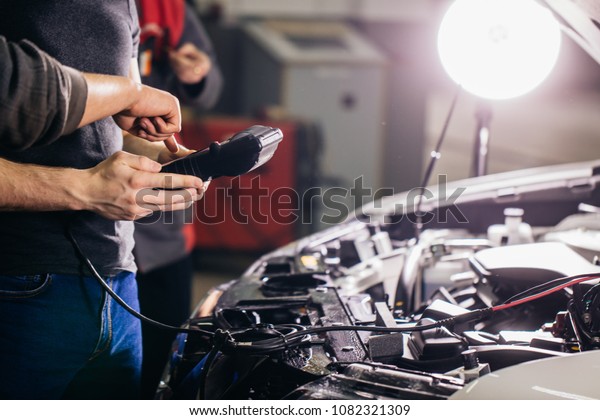 Car mechanic using electrical tool for testing car\
system in garage repair