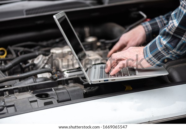 Car\
mechanic using laptop for checking car\
engine