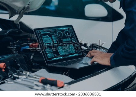 Car mechanic using laptop computer examining tuning fixing repairing car engine in garage.Car repair service and maintenanc concept.