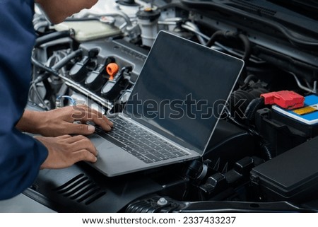 Car mechanic using laptop computer examining tuning fixing repairing car engine in garage.Car repair service and maintenanc concept.