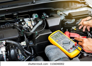 Car mechanic is using a multimeter with voltage range measurement to check the voltage level of the car battery.
