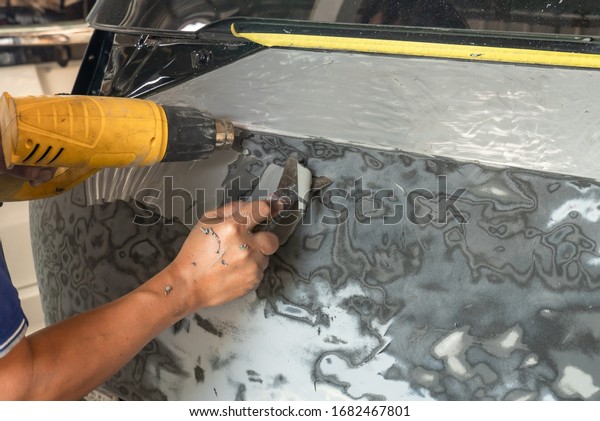 Car mechanic is using\
putty knife ,Scraping the car paint ,By using a hot dryer, it helps\
to be easy.