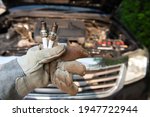 Car mechanic wearing gloves holding old spark plugs to replace new spark plugs according to the maintenance plan
