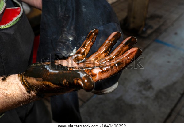 A car mechanic wipes dirty hands, stained with\
used oil with a cloth.