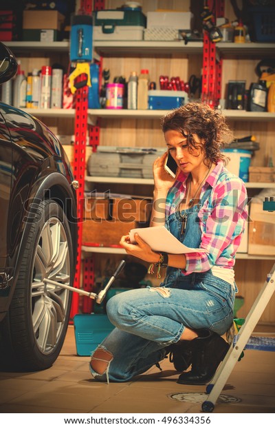 car mechanic woman in blue overalls talking on the
phone near a car in the interior of the garage. instagram image
filter retro style
