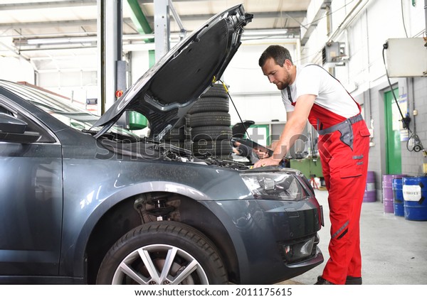 car mechanic in work clothes checks engine from\
a car in a workshop