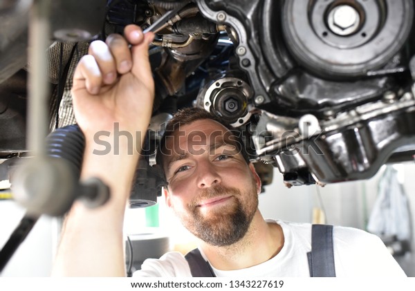 car mechanic in work clothes works in a workshop and\
repairs a vehicle 