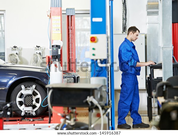 car mechanic working with computer during\
suspension adjustment and automobile wheel alignment work at repair\
service station