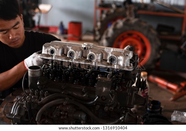 The car mechanic\
is working with the car engine in the garage, repairing the tractor\
for agriculture.