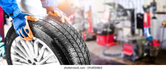 Car Mechanic Working In Garage And Changing Wheel Alloy Tire. Repair Or Maintenance Auto Service. Wide Banner, Panorama Photo.