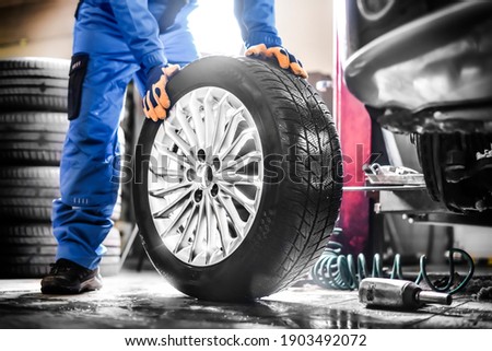 Car mechanic working in garage and changing wheel alloy tire. Repair or maintenance auto service.