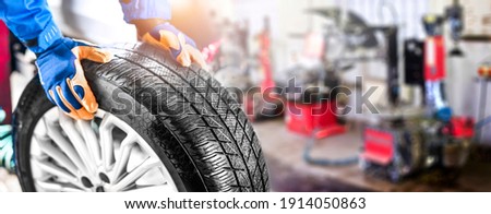 Car mechanic working in garage and changing wheel alloy tire. Repair or maintenance auto service. Wide banner, panorama photo.