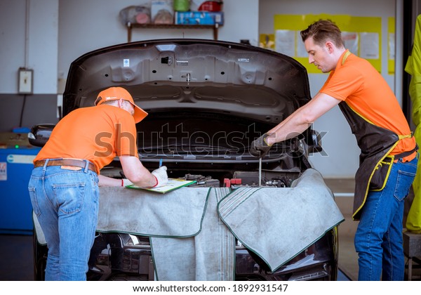 Car mechanics open hood discussion to repair and\
check car problem system by note detail in document maintenance and\
fixed in garage.