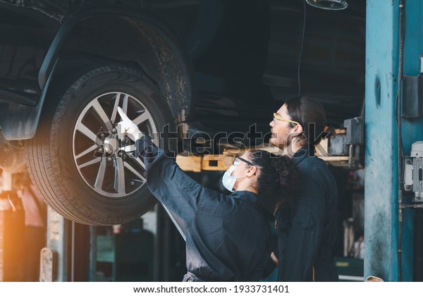 Car mechanics under checking car\
wheels at garage for maintenance or charge a new new wheel ,they\
wearing safety uniform, glasses and face mask to work.\
