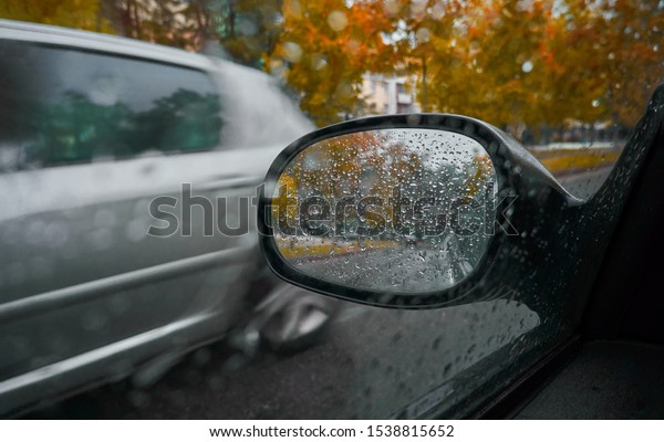 Car mirror with raindrops and reflection of trees and\
a second car