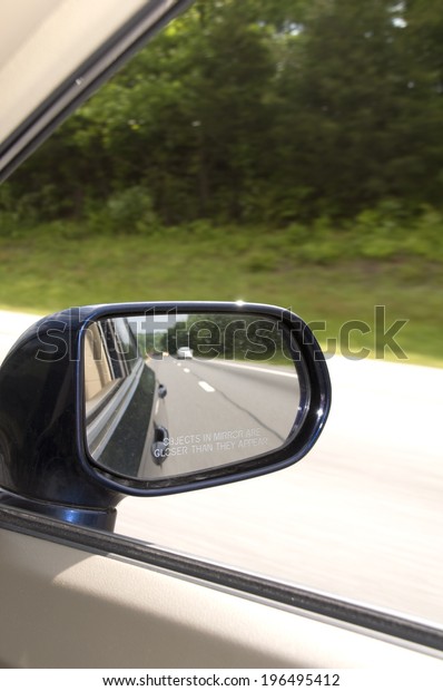 A car mirror\
reflecting the road behind\
it.
