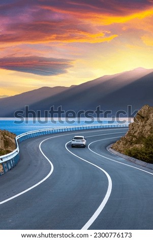 Car in motion in the highway landscape under the coastal road. Road landscape at colorful sunset. Car driving on the highway. Nature scenery on sea beach. Travel journey for summer trip on road.