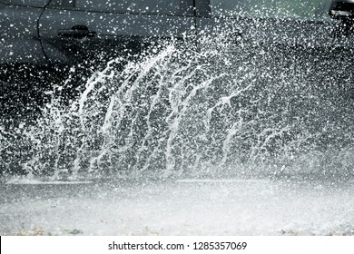 Car Motion Through Big Puddle Of Water Splashes From The Wheels On The Street Road. Water Splash Rain Texture