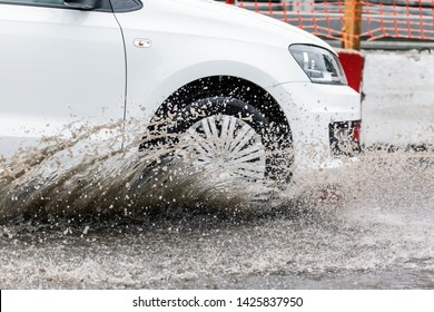 Car Motion Through Big Puddle Of Water Splashes From The Wheels On The Street Road. Water Splash Rain Texture