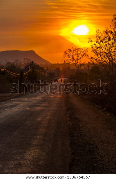 Car and motorbike silhouette\
driving on a scenic road in orange sunset in countryside of\
Laos