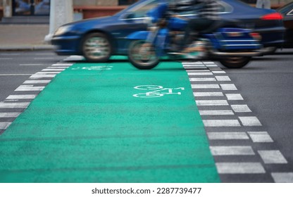 Car and motorcycle driving through bicycle lane marked with paint. Pedestrian crossing, bicycle lane sign marked on asphalt. Motocyclist crossing bike path lane. Danger for cyclists when crossing road