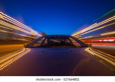 The Car Moves At Great Speed At The Night. Blured Road With Lights With Car On High Speed. The View From The Front To Back.