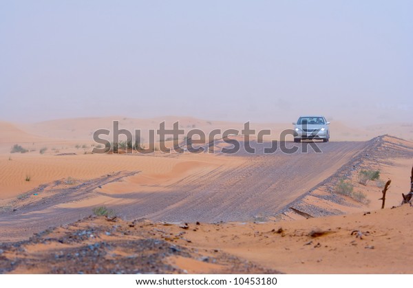 A car moving along a desert road. Visibility\
slightly limited by sand in\
midair.