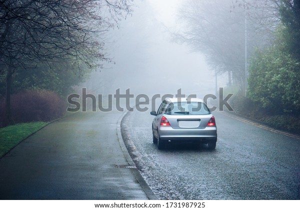 A car moving in a\
fog in a city - concept of a dangerous hazardous driving\
conditions, limited\
visibility
