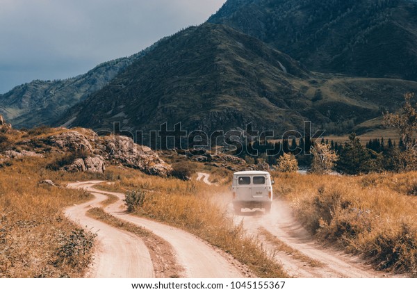 The car is moving forward along a\
dirt road among the mountains and hills. Mountain\
Altai.