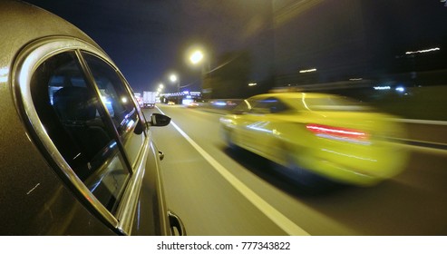 The Car Is Moving At High Speed On The Night Road In The City. Side Camera Location On The Car Body.