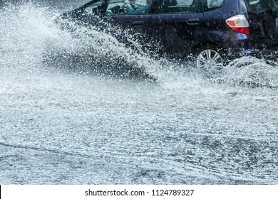 Car Moving With High Speed Through Water Puddle On Flooded City Road During Heavy Rain