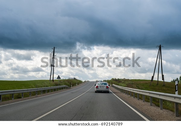 Car moving up the hill on country road on overcast\
summer day in Latvia