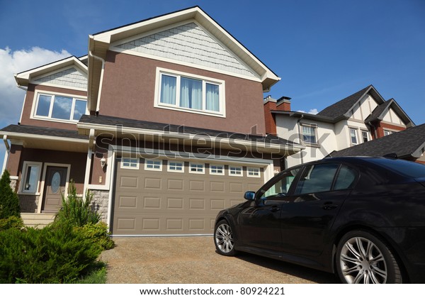Car near the garage of new two-storied brown cottage\
with white roof