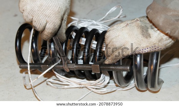 Car new coil spring\
tightening with a tool equipment by men\'s hands in work gloves -\
car repair service