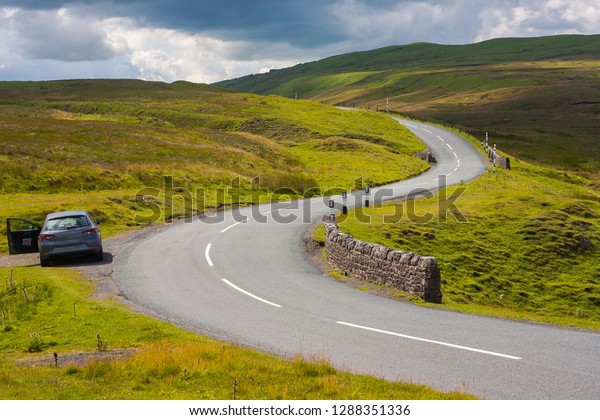 A car next to the road, parking\
in an \'S\' curve. English Landscape, quick rest next to\
road.