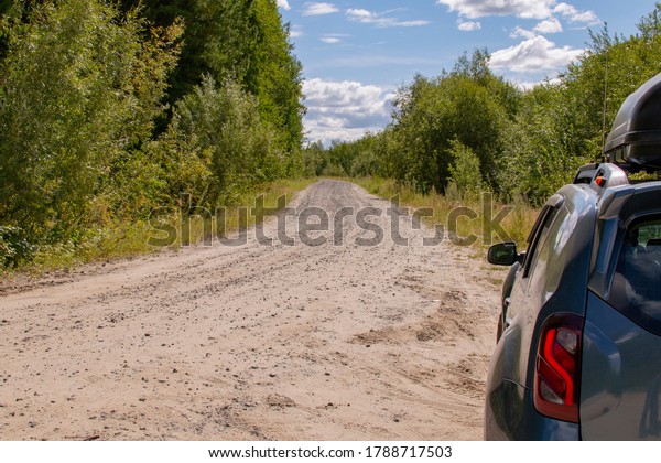 the car is next to a sandy road in the middle of\
the forest