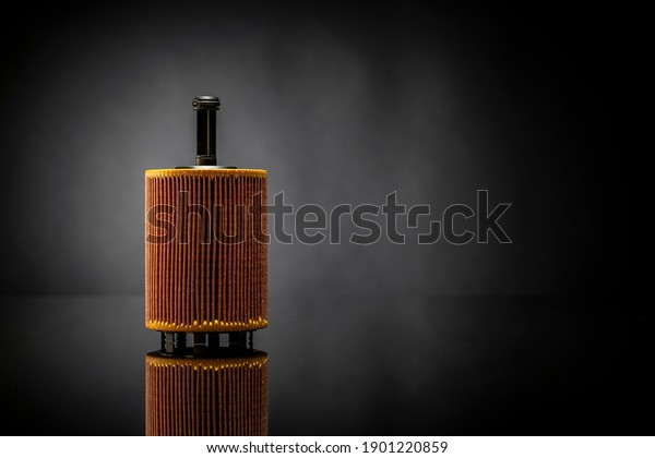 Car OIL filter used for car maintenance\
placed on black reflexive glass isolated on black background on the\
left side with negative space on the right.\
