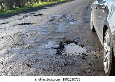 A Car On A Bad Bumpy Road With Potholes, Destroyed Asphalt And Puddles. Water Pits On Broken Asphalt. Spring And Autumn Problems For Drivers.