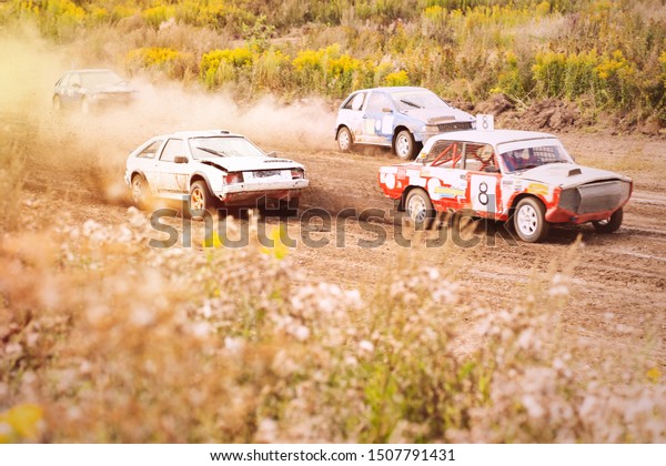 Car on dirt track. Racing cars in the fresh air\
with dust. Four cars at high speed are fighting for victory to the\
finish line.