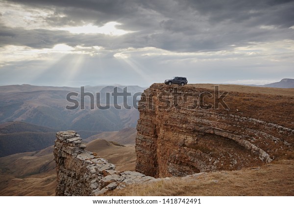 Car on the edge of a rock cliff against the\
sky. Extreme travel and freedom. Landscape with sandy rocks in the\
shape of an amphitheater.
