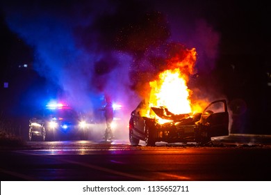 Car on fire at night with police lights in background no one