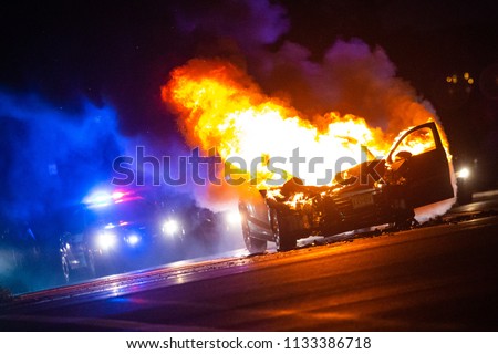 Car on fire at night with police lights in background no one