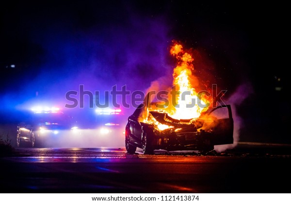 Car on
fire at night with police lights in
background