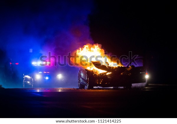Car on\
fire at night with police lights in\
background