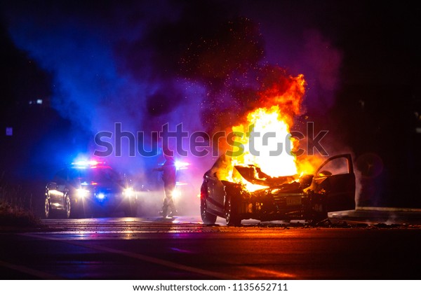 Car on fire at night with police lights in background\
no one