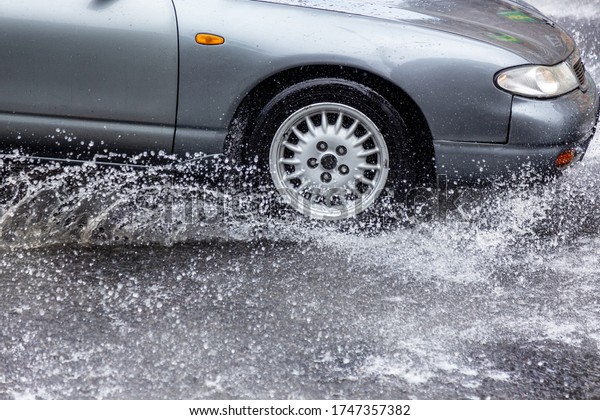 Вriving car on flooded road during flood caused by
torrential rains. Cars float on water, flooding streets. Splash on
car. Flooded city road with large puddle.  Flooding after heavy
rains at city