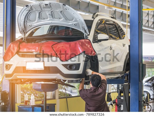 Car on lift to repair suspension in the
garage with mechanic working underneath lifted car to change wheel
hub and maintenance repair at service station 
