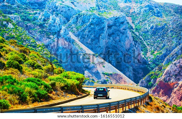 Car on the road at Buggerru in Sardinia Island in\
Italy summer. Transport driving on the highway of Europe. Holiday\
View on motorway. Cagliari province. Mountains on background. Mixed\
media.